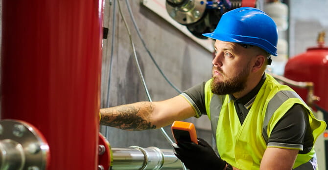 Man in hard hat sitting on floor of boiler room examining pipes