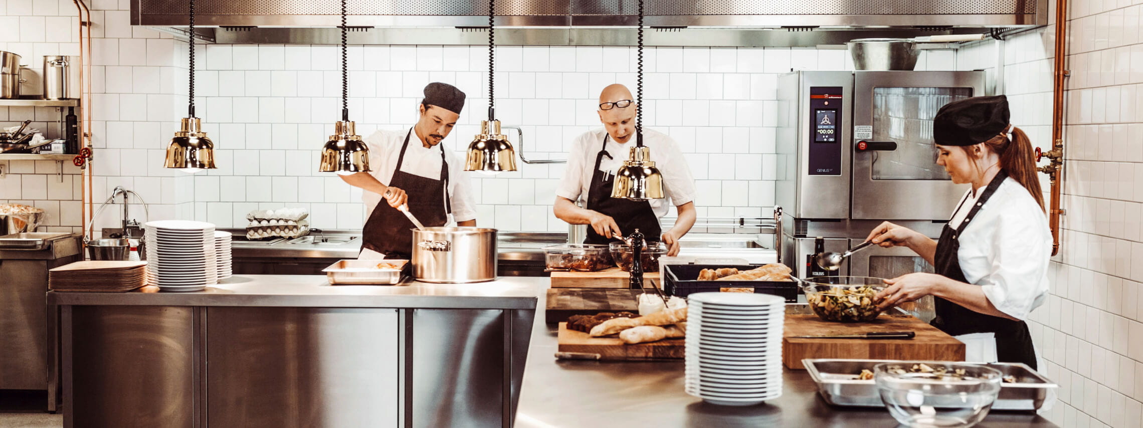Three cooks prepare food in a modern commercial kitchen.