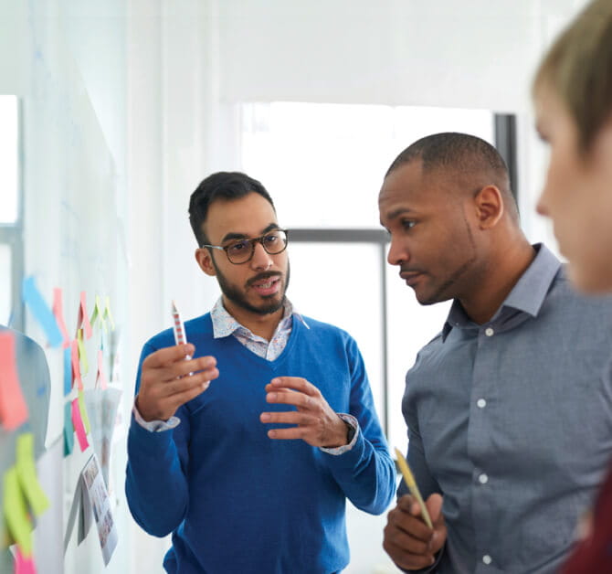Three men brainstorming at a whiteboard in an office