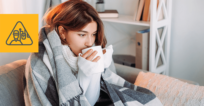A woman drinking hot beverage sitting on a couch with blanket