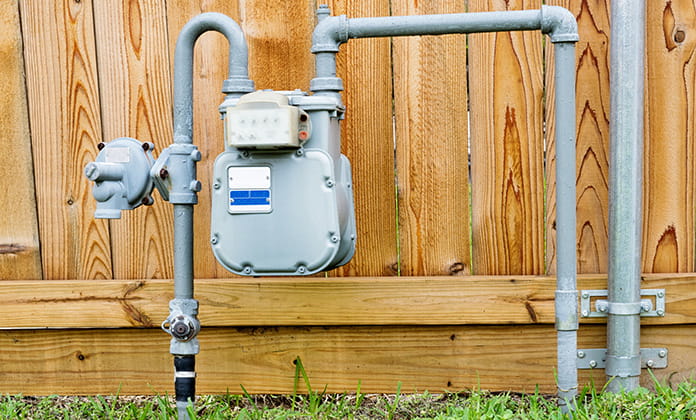 Natural gas meter in residential suburban backyard with wooden fence in background. 