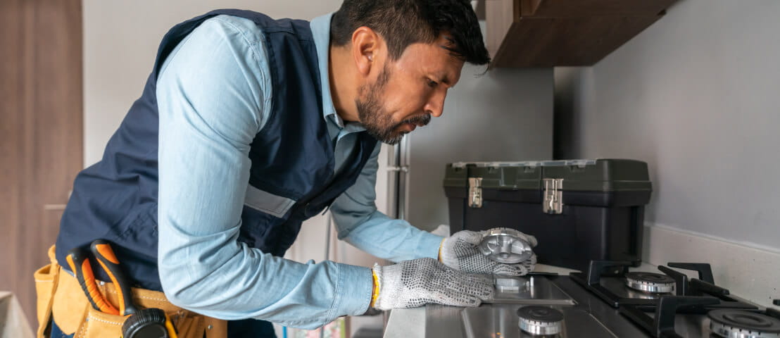 A worker wearing gloves and a utility belt inspecting a gas stove.