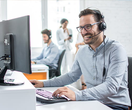 Smiling customer support operator with hands-free headset working in the office.