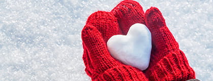 Hands in a knitted mitten with a snow heart.