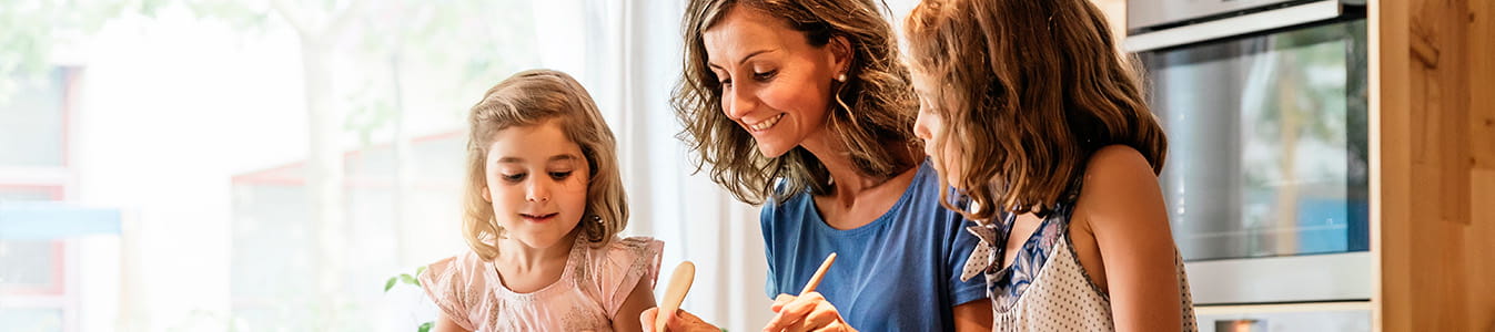 Little sisters cooking with her mother in the kitchen.