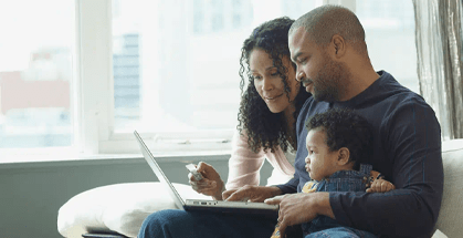 Couple sitting on couch looking at laptop with a child