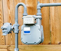 Natural gas meter in residential suburban backyard with wooden fence in background.
