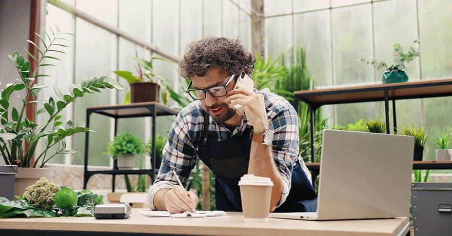Businessman talking on cellphone while writing down order details. 