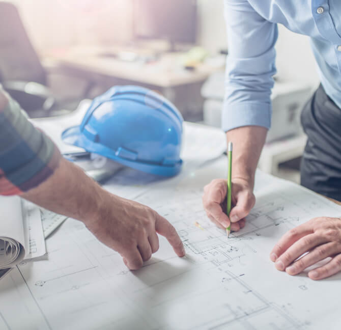 Hands of two men pointing at an architectural blueprint on a table