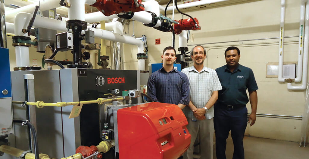 Three men standing beside boiler room equipment