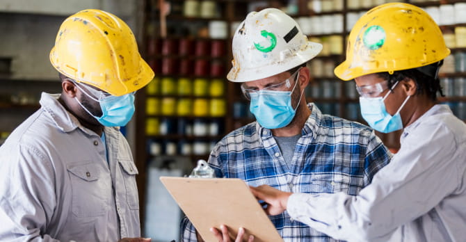 3 workers with hard hats and face masks, looking at clipboard