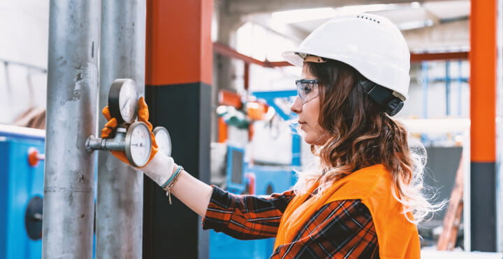 A technician examines a meter in an industrial mechanical room.