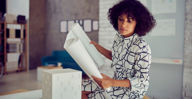 Woman sitting in office holding blueprint and examining 3D model