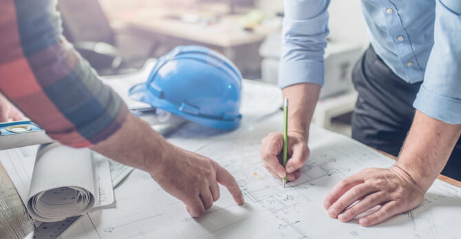 Hands of two men pointing at an architectural blueprint on a table
