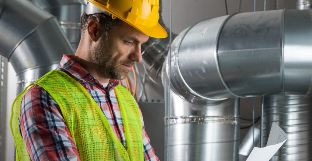 A man in a hard hat examining a blueprint in a factory