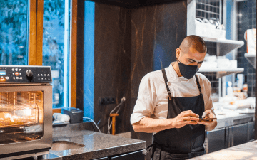 A person wearing a face mask and apron working in a kitchen.