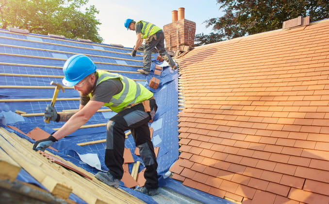 Two workers wearing safety equipment while applying shingles to a roof. 