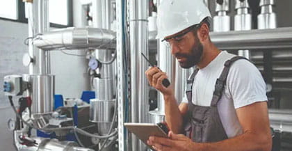Engineer holds tablet and walkie-talkie in boiler room.