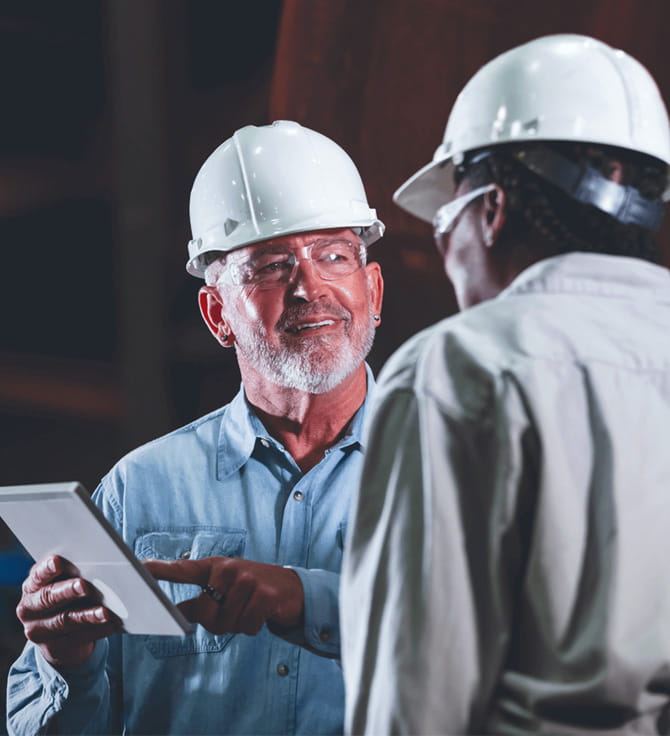 A person wearing hardhats and holding a tablet.
