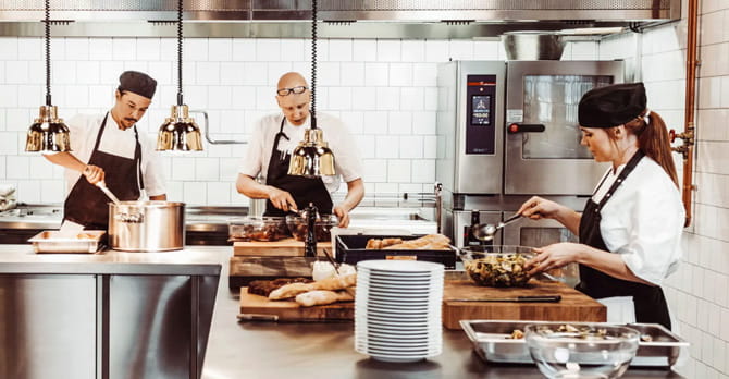 Three cooks prepare food in a modern commercial kitchen.