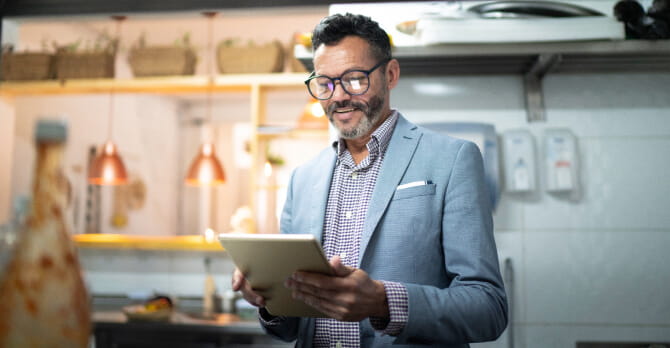 Man in suit standing in kitchen looking at tablet