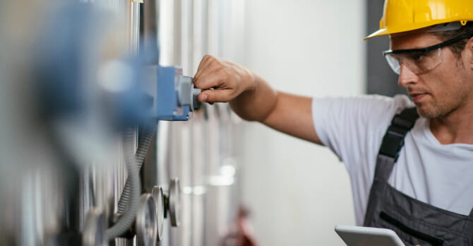 Man at work wearing a yellow hard hat and safety goggles, while holding a tablet.