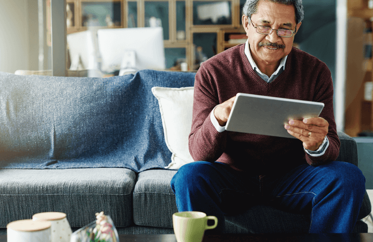Senior man sitting on his couch while using a tablet