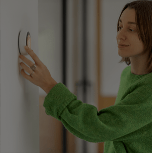 Woman controlling temperature with a smart thermostat mounted on the wall