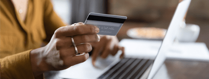 Hand holding a credit card by a laptop.